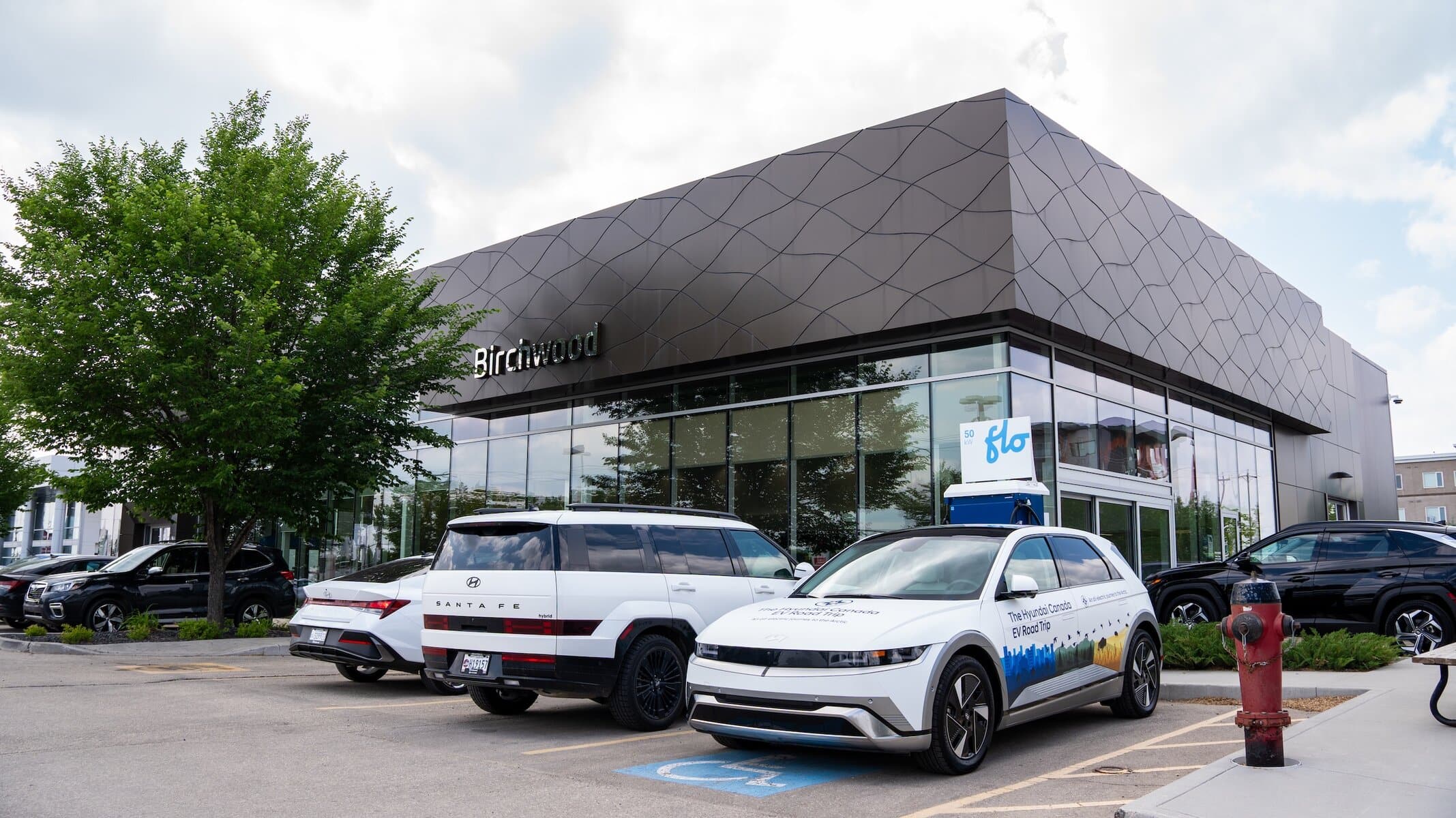 Exterior of Birchwood Hyundai featuring modern architecture with a patterned facade, EV charging station, and Hyundai vehicles—including a branded IONIQ 5—parked out front.